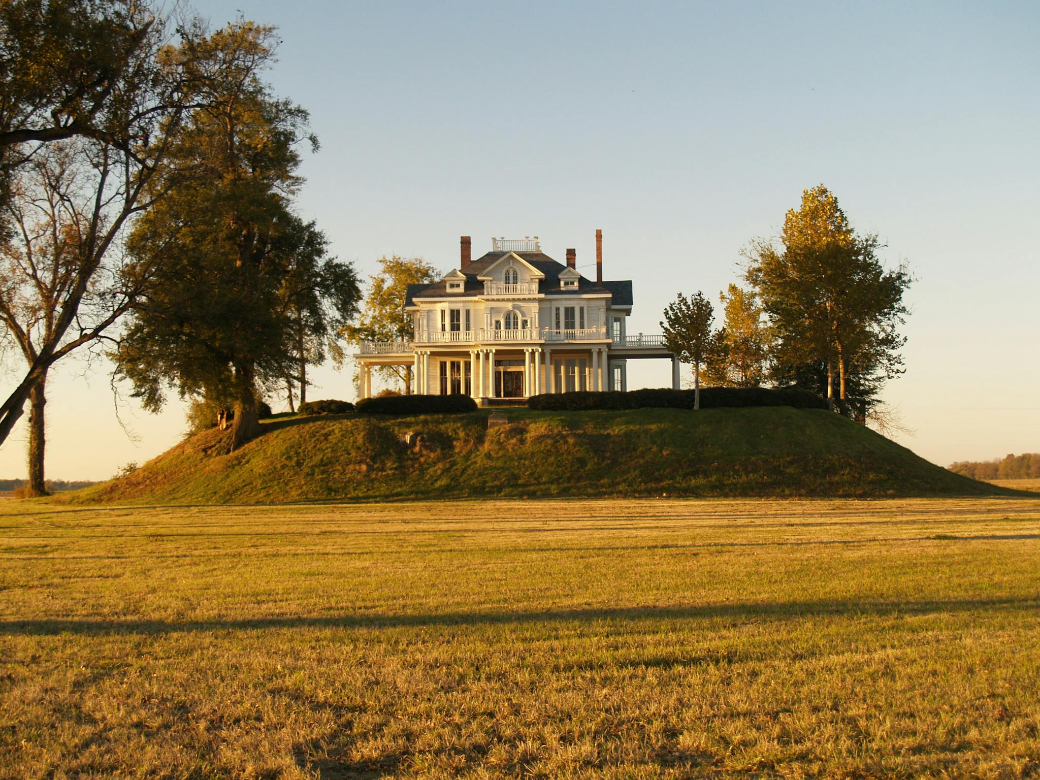 Majestic colonial style mansion situated on a scenic hilltop at sunset.
